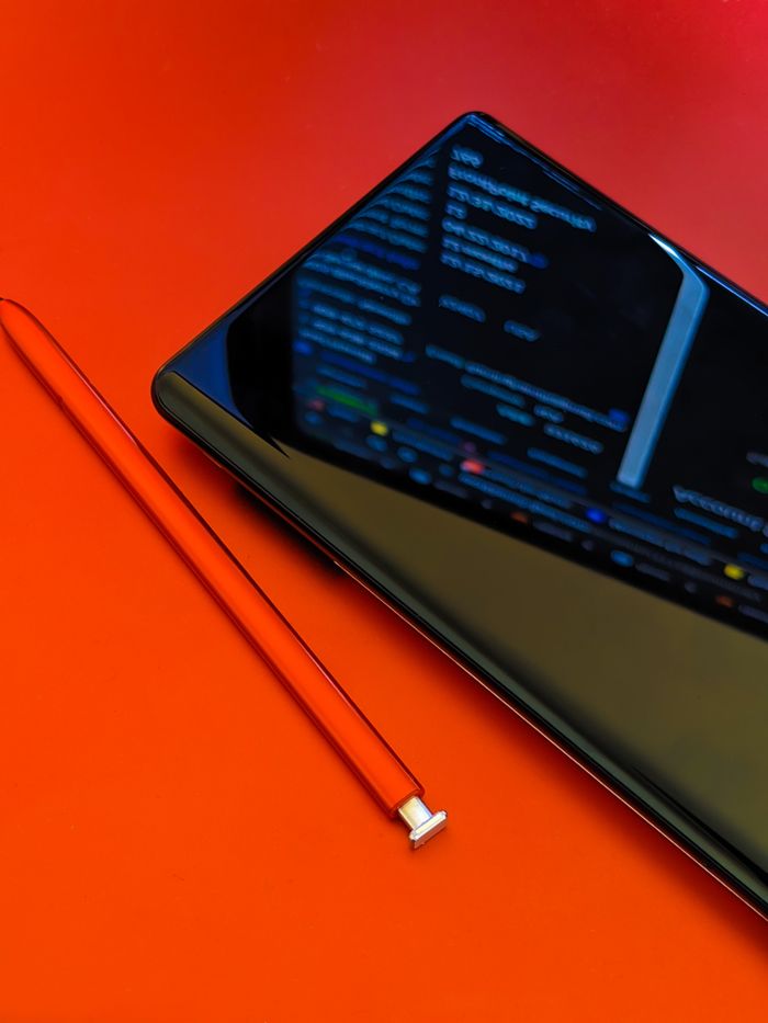 Detailed view of a smartphone with a stylus resting on a vivid red background, highlighting contemporary technology.